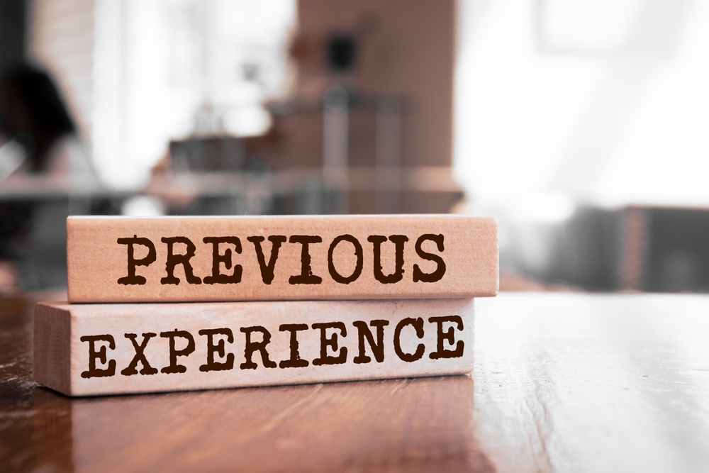 Two wooden blocks stacked on a table, each displaying bold text that reads PREVIOUS EXPERIENCE, with a blurred background