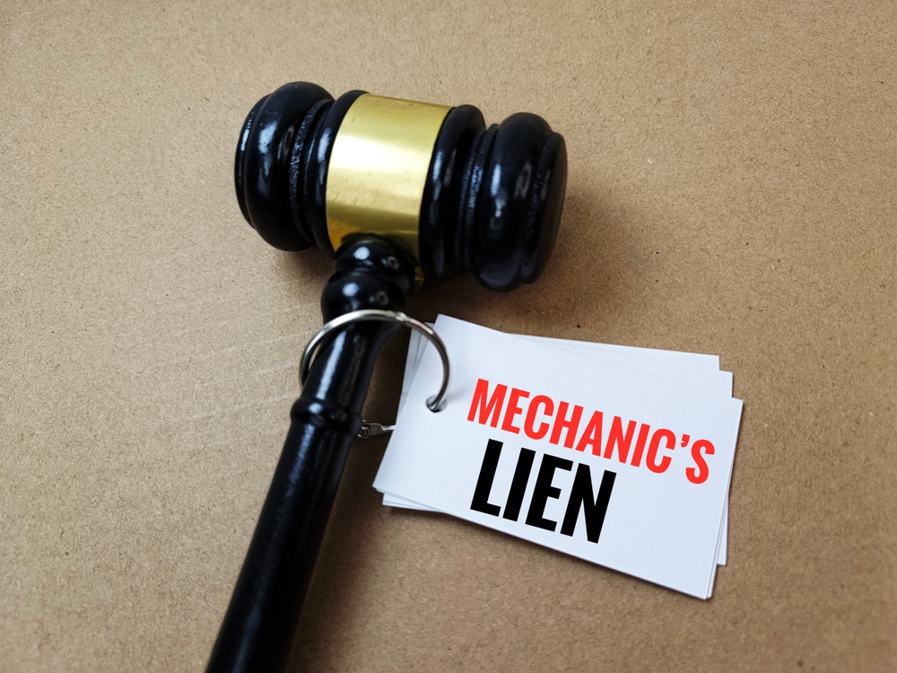 Black gavel with a gold band rests on cards labeled MECHANIC’S LIEN, symbolizing legal or construction-related financial claims