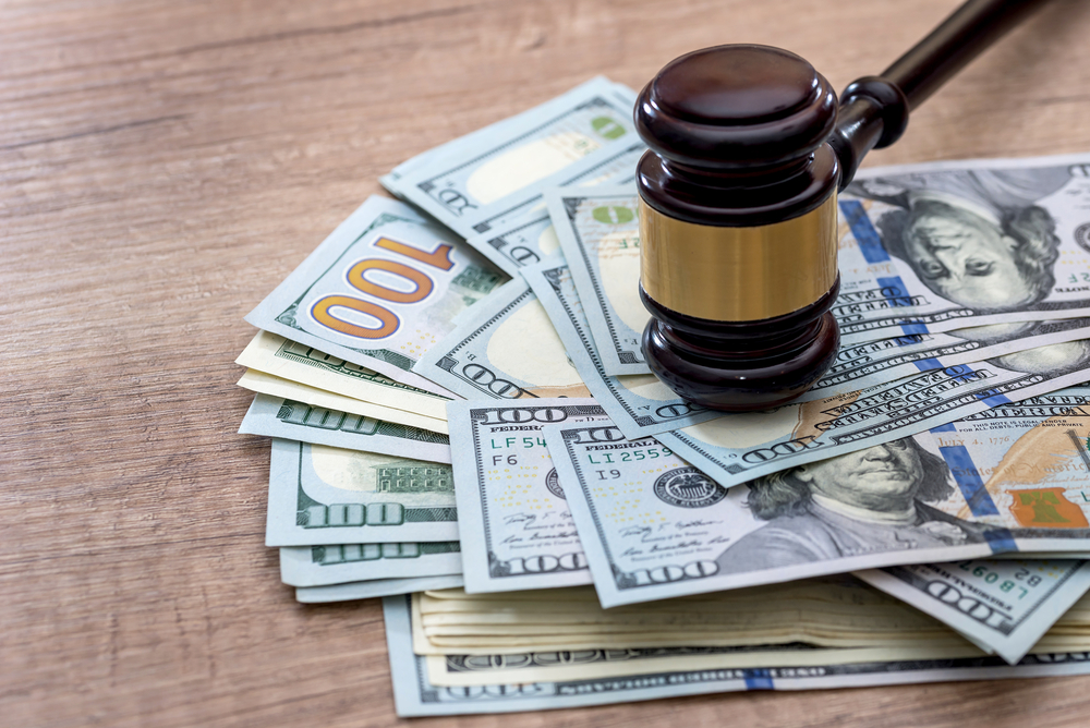 Stack of U.S. hundred-dollar bills with a judge's gavel resting on top, symbolizing legal or financial judgment