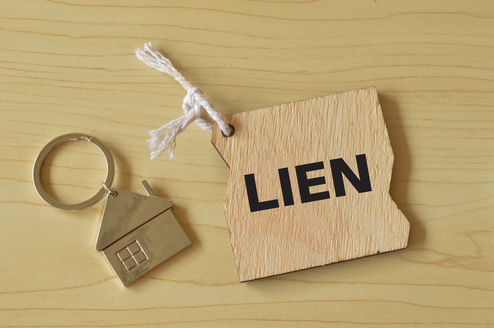 Close-up of wooden tag labeled LIEN tied with string next to metal house keychain on light wood surface